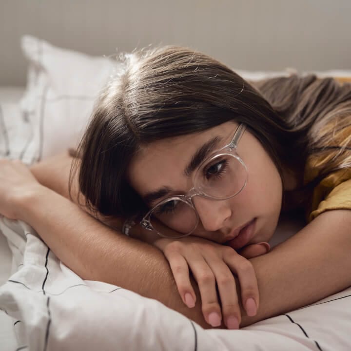 Sad caucasian teenage girl lying on bed and looking away with anxiety